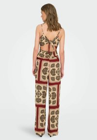 Ensemble léger en deux pièces comprenant un haut court beige avec un nœud dans le dos et un pantalon large, orné de motifs floraux noirs et d'accents bordeaux.