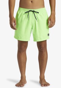 Bañador verde lima con cintura elástica, cordón negro, bolsillos laterales y un pequeño parche de logo en el dobladillo inferior.
