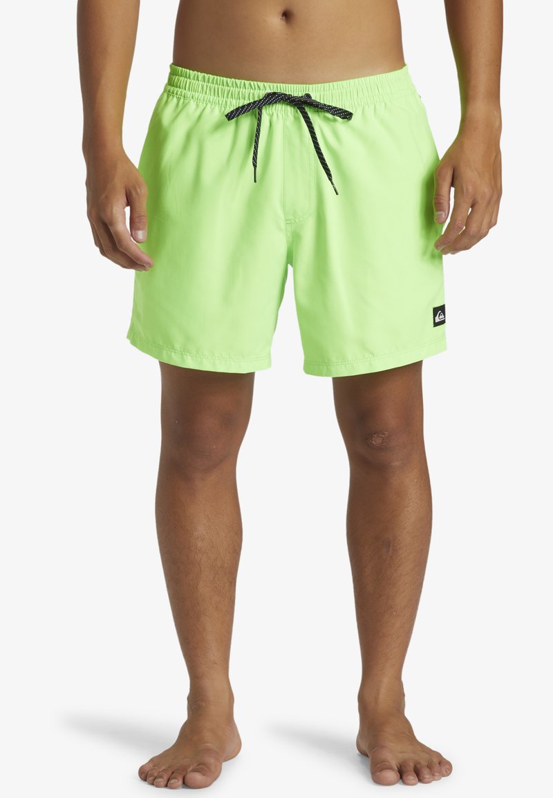 Bañador verde lima con cintura elástica, cordón negro, bolsillos laterales y un pequeño parche de logo en el dobladillo inferior.