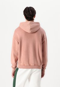 Sudadera rosa de corte relajado, con capucha ajustable y puños acanalados, fabricada con material suave, vista desde la parte de atrás.