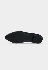 Semelle d'une chaussure plate noire à bout pointu avec des motifs de grip texturés et la marque "GABOR" sur un fond blanc uni.