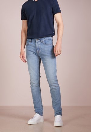 Mørkeblå, ribbede kortærmede V-hals skjorte parret med lyseblå slim-fit jeans og hvide sneakers, sat mod en neutral baggrund.