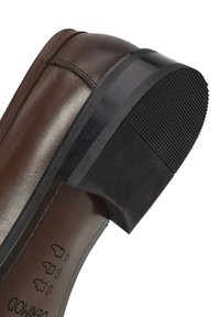 Zapato de vestir de cuero marrón con tacón de goma negro y detalles cosidos, mostrando la suela y el forro interior con símbolos de materiales.