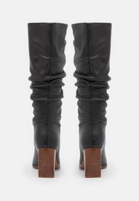 Bottes noires montant jusqu'aux genoux en cuir, présentant un design froncé, un bout carré et des talons carrés en bois avec une finition texturée.