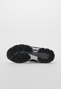 Semelle de chaussure de sport noire avec caoutchouc texturé pour une meilleure adhérence, présentant un design rainuré et un amorti visible. Accents gris le long de l'arche.