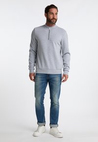 Grå sweatshirt med lynlås ved kraven, kombineret med lyseblå jeans og hvide sneakers. Stoffet har en glat tekstur og en afslappet pasform.