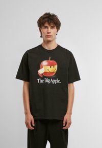Camiseta de algodón negra con un gran gráfico de una manzana roja con cara sonriente y el texto "La Gran Manzana" impreso debajo en blanco.