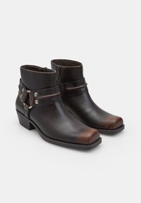 Botas de tobillo de cuero negro con cremallera, con una correa horizontal y detalles en plata. Punta cuadrada y tacón bajo en bloque. Textura suave.