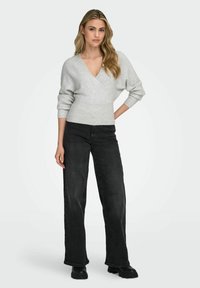 Jasnoszary, prążkowany sweter z głębokim dekoltem w kształcie V i balonowymi rękawami, zestawiony z czarnymi, długimi jeansami z wysokim stanem i grubymi czarnymi butami.