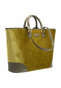 Borsa tote in velluto verde con motivo in rilievo, dettagli in pelle marrone, doppi manici e un'etichetta con logo frontale. Forma strutturata con una texture morbida.