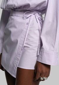 Chemise en tissu rayé violet avec un lien à la taille, présentant un devant boutonné et des manches longues avec de larges poignets.