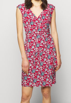 Ærmeløs rød slå-om-kjole med blåt og hvidt blomsterprint båret af en kvinde, beskåret fra nakken til midt på låret, ensfarvet lys baggrund.