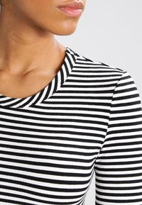 Närbild av en person som bär en långärmad svart- och vitrandig tröja med rundad halsringning.