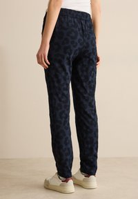 Pantalons de survêtement bleu marine en tissu doux avec un motif léopard noir, dotés d'une taille élastique et de deux poches arrière. Coupe et design décontractés.