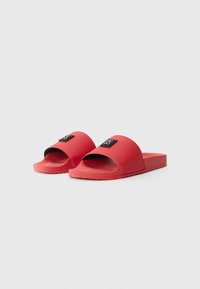 Røde rutsjesandaler med en glat gummioverdel, bred rem, tekstureret sål og en sort logoaccent foran.
