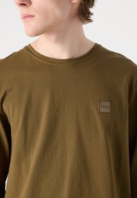 Smaragdgrüne Longsleeve-Bluse aus weicher Baumwolle. Verfügt über ein kleines quadratisches Logo-Patch mit "BOSS" auf der Brust. Glatte Textur, Rundhalsdesign.