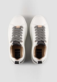 Sneakers bianchi a basso profilo con lacci grigi, linguette nere sul tallone e dettagli metallici in oro rosa, visti dall'alto su uno sfondo chiaro.