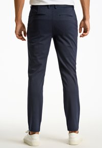 Pantalon ajusté bleu marine avec une texture lisse, coupe slim et poches latérales inclinées, associé à des baskets blanches et un t-shirt blanc uni.