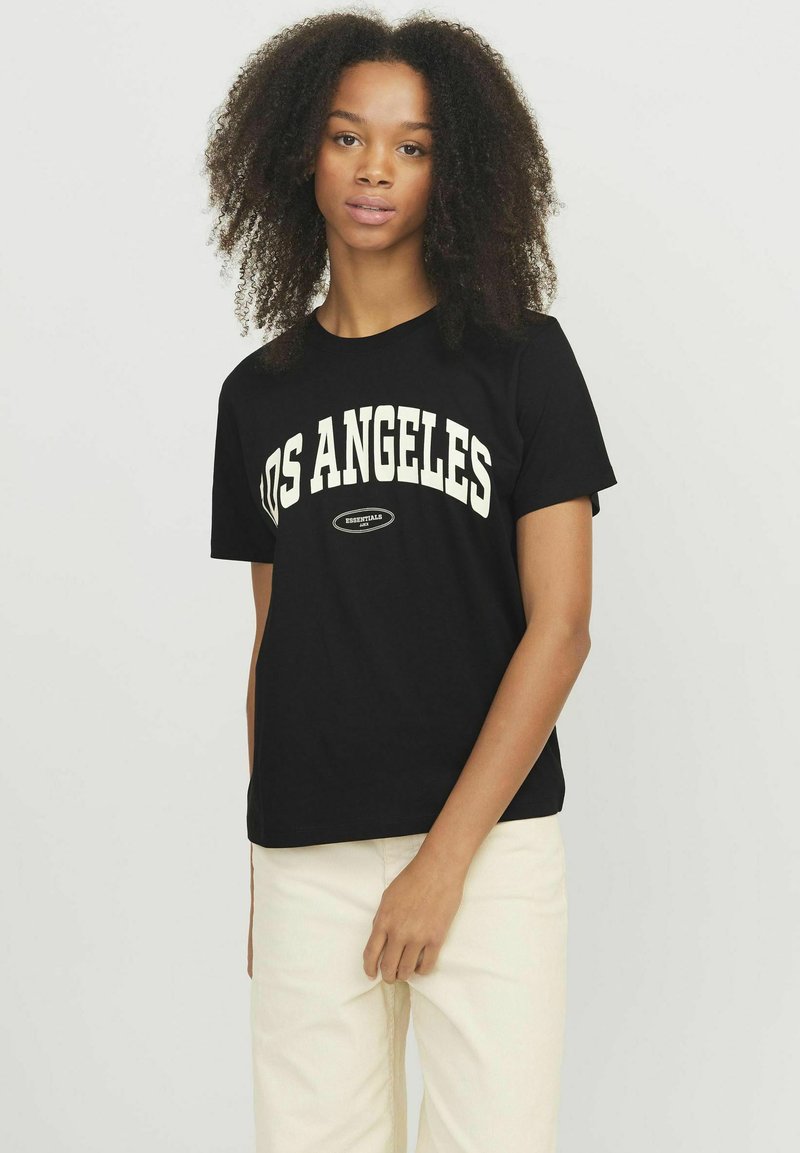 T-shirt in cotone nero con "LOS ANGELES" stampato in grassetto lettere color crema. Maniche corte, collo a giro, abbinato a pantaloni chiari.