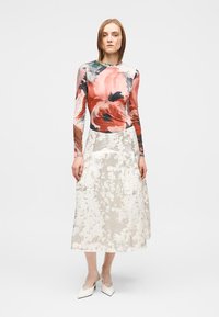 Langarmshirt met een meerkleurig bloemmotief en een witte, getextureerde midirok met een bloemendessin, gecombineerd met witte hakken.