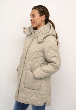 Beige quiltet jakke med hætte, der har lynlås lukning, sidelommer og geometrisk mønster. Stoffet fremstår glat og blødt.
