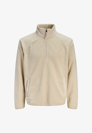 Beige fleece pullover with a half-zip collar, raglan sleeves, side pockets, and a soft textured finish. Logo detail on the chest.