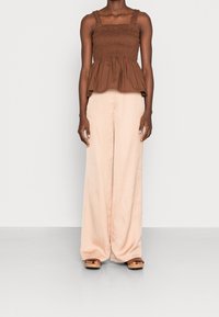 Haut péplum smocké marron avec larges bretelles, associé à un pantalon large couleur pêche claire ; tissu lisse, coupe décontractée et détails de conception minimalistes.