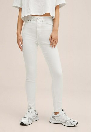 Weiße, hoch geschnittene Skinny Jeans mit Knopfverschluss, glatter Textur und enger Silhouette, kombiniert mit hellgrauen Sneakers.