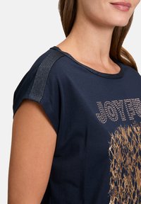 Navy blue top with short sleeves, featuring metallic thread accents and a golden graphic design on the front, smooth cotton texture.