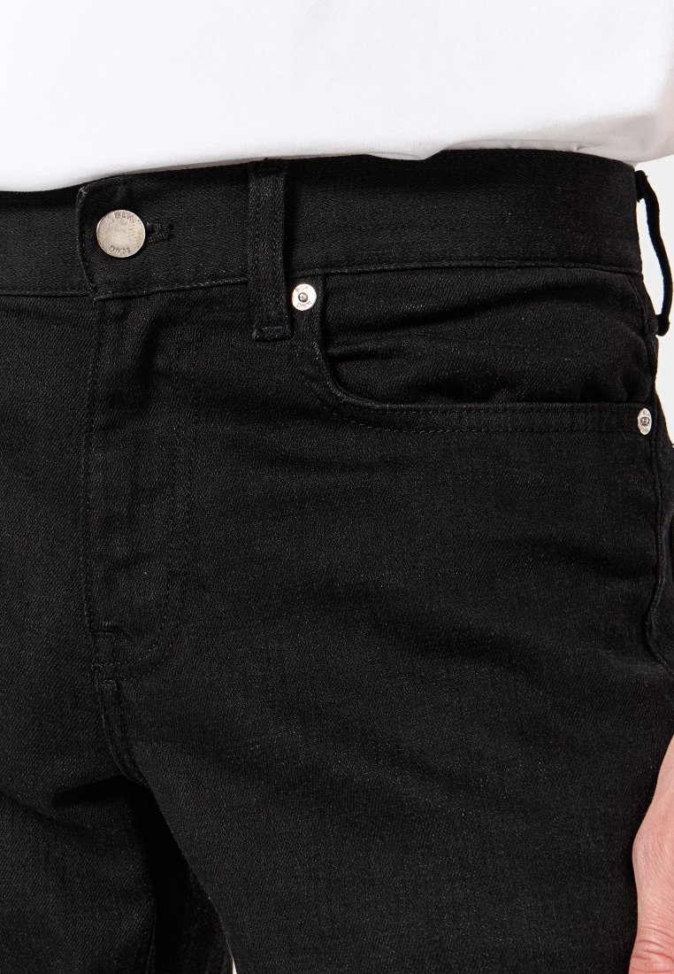 Schwarze Denim-Jeans mit einem klassischen Fünf-Taschen-Design, silberner Hardware und einer glatten Textur. Nahaufnahme des Taillenbunds und des Taschenbereichs.