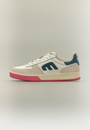Baskets basses avec tige blanche et beige, logo bleu et accent talon, semelle intermédiaire crème et semelle extérieure rouge tachetée, vues de côté.