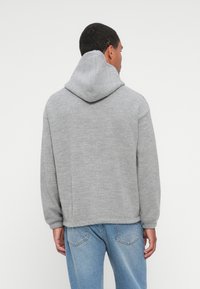 Sweat-shirt à capuche gris avec une finition texturée, épaules tombantes et ourlet côtelé. Porté avec un jean bleu clair, vu de dos.