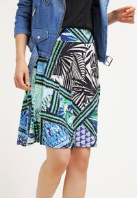 Jupe évasée arborant un motif vibrant de feuilles et géométrique en bleu, vert et noir. Fabriquée en tissu léger avec une texture lisse.