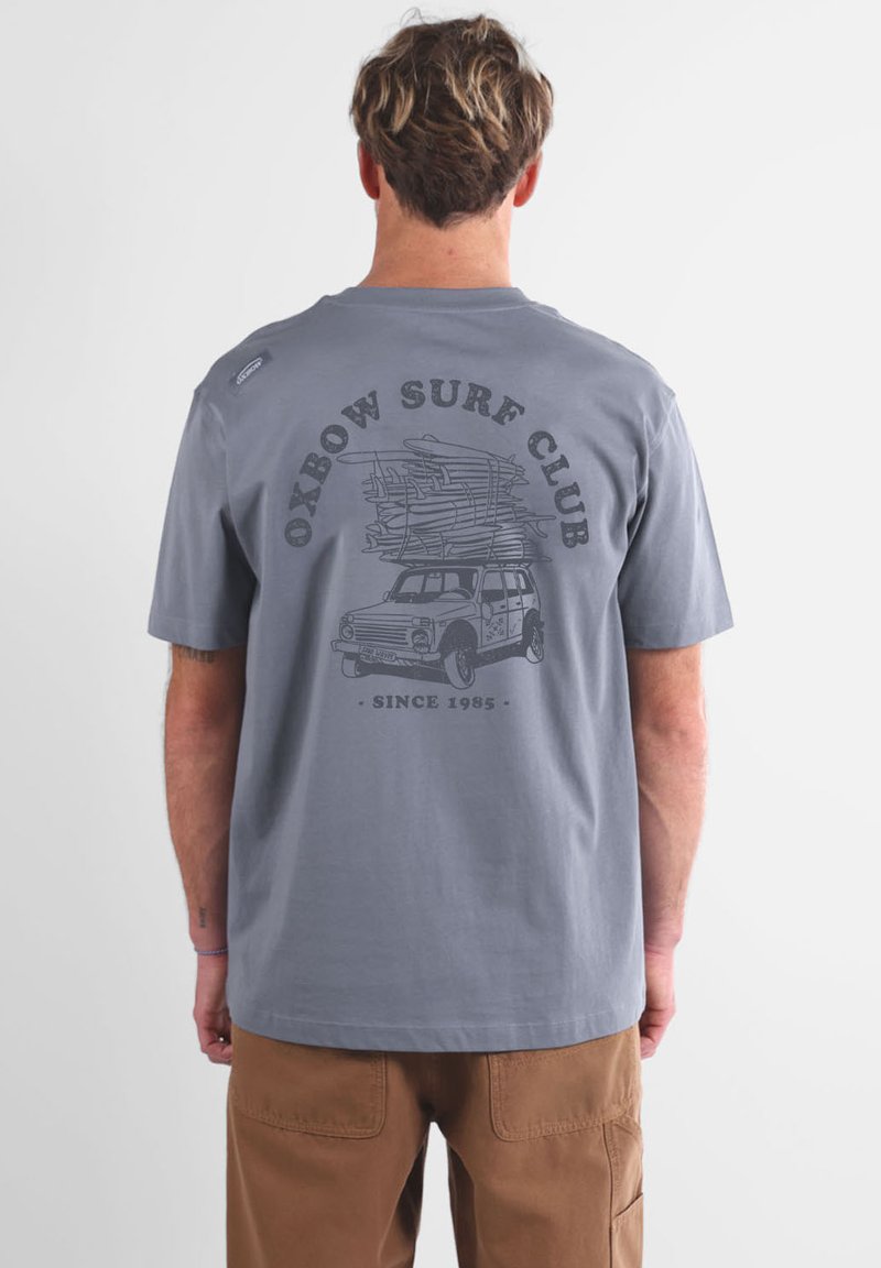 T-shirt gris à manches courtes avec une illustration graphique d'une camionnette portant des planches de surf à l'arrière, et le texte "Oxbow Surf Club" au-dessus.
