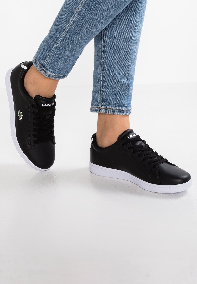 Svarta syntetläder sneakers med vita gummisulor, utrustade med svarta snören och en liten färgad logotyp på utsidan.