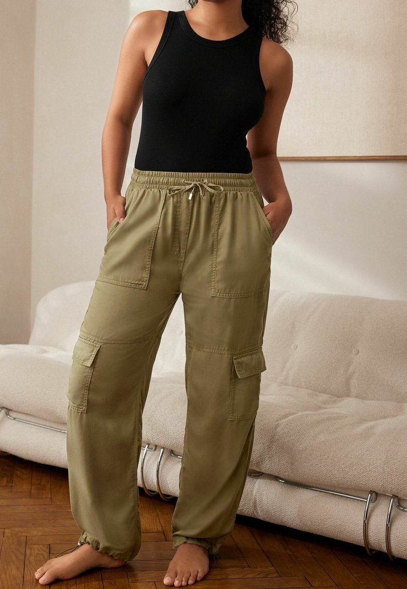 Zwart tanktop gecombineerd met olijfgroene cargobroek met een koord in de taille, zijzakken en elastische boorden, gelegen in een gezellige binnenruimte.