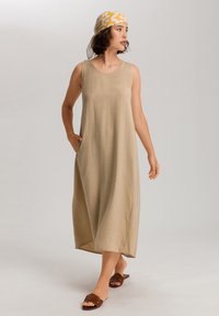 Beige lněné šaty bez rukávů s uvolněným střihem, bočními kapsami a ke kolenům. Nosené s hnědými plochými sandály a vzorovaným šátkem.