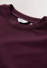 Bordeauxrode crewneck T-shirt van katoen, met een zachte textuur en zichtbare stikdetails. Label geeft aan "NEXT - Relaxed Fit."