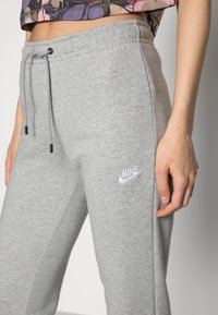Pantalons de survêtement Nike gris en tissu doux, avec une taille à cordon, des poches latérales et un logo Nike blanc brodé sur la cuisse.