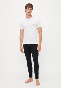 Vit kortärmad T-shirt med röd "HUGO" logotyp på vänster bröst, kombinerad med tajta svarta leggings. Enkelt design; mjuk tygets struktur.