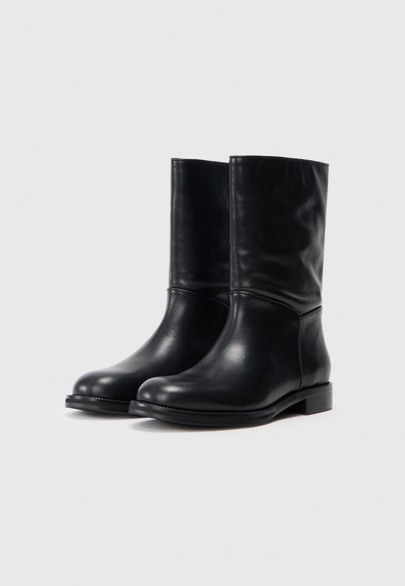 Bottines noires en cuir avec un bout légèrement arrondi, texture lisse et un petit talon empilé. Présentent un design simple avec une finition soignée.