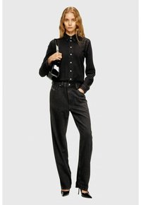 Camicia in denim nero con chiusura a bottoni, abbinata a jeans neri a vita alta. Completano il look décolleté nere e una borsa nera lucida.