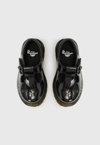 Chaussures Mary Jane en cuir verni noir avec un embout arrondi, une boucle réglable, une doublure rembourrée et une semelle en caoutchouc noir texturée.