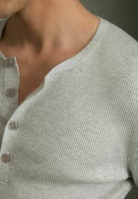 Tricou henley gri cu nervuri, cu guler în V, trei butoane și mâneci scurte. Textura materialului este moale și ușor texturată.
