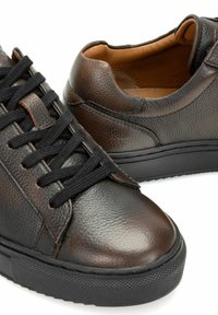 Ciemnobrązowe teksturowane skórzane buty sportowe z czarnymi sznurowadłami i grubymi czarnymi gumowymi podeszwami, pokazujące widoki z przodu i z boku na białym tle.