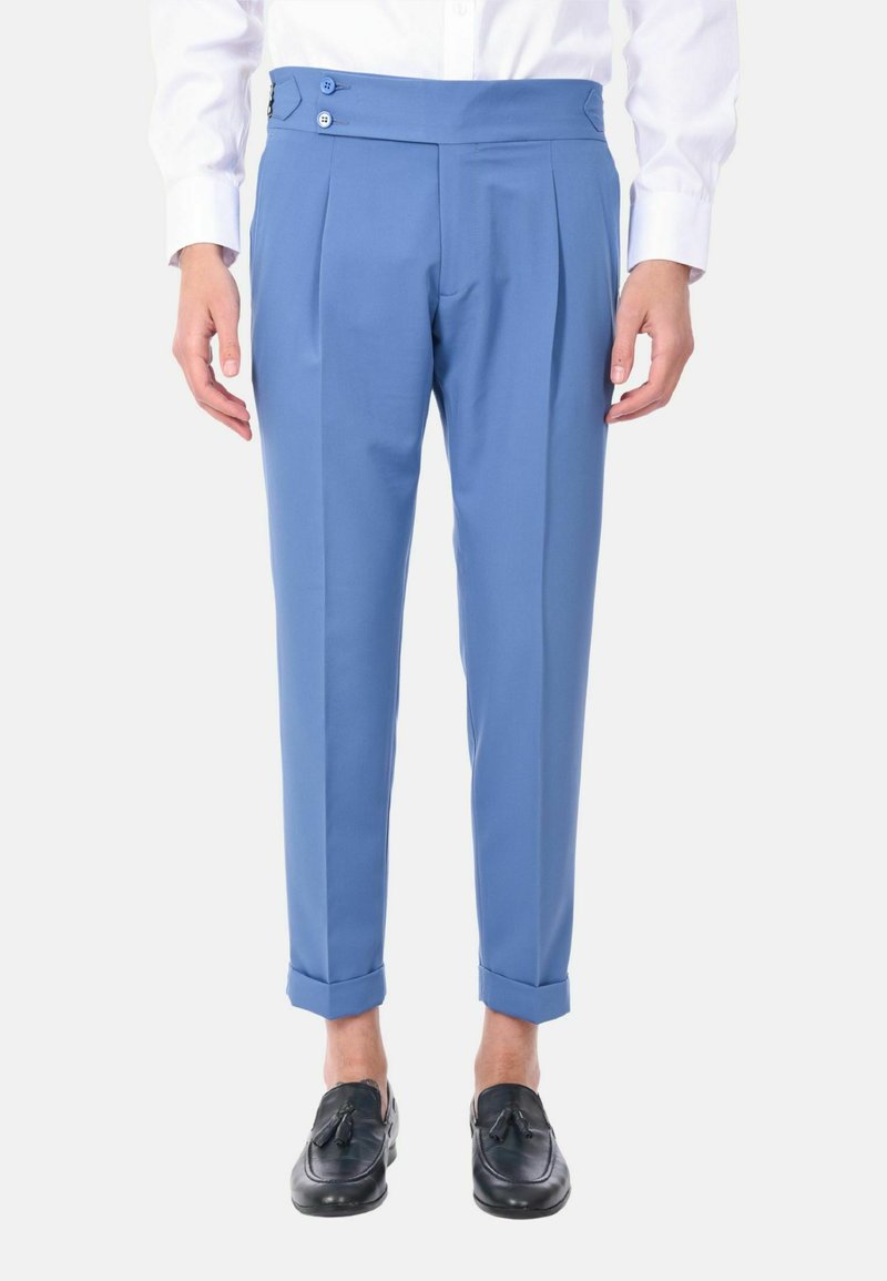 Pantaloni su misura blu chiaro con vita alta, due pieghe laterali e due dettagli con bottoni; orlo risvoltato; indossati con mocassini neri.