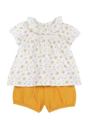 Haut à manches courtes à motif floral blanc avec col à volants ; associé à un short jaune à pois. Tissu doux, design décontracté.