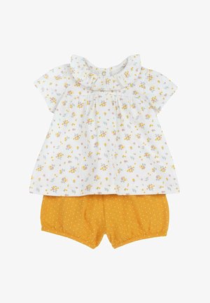 Haut à manches courtes à motif floral blanc avec col à volants ; associé à un short jaune à pois. Tissu doux, design décontracté.