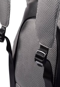 Mochila de malla gris con correas acolchadas, herrajes negros y una superficie texturizada para transpirabilidad y comodidad. Detalle de cremallera visible.