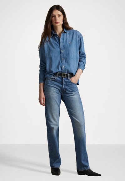 Cămașă din denim de culoare albastru deschis cu guler căptușit, asociată cu blugi drepți de culoare albastru mediu. Curea neagră și botine negre cu vârf ascuțit.